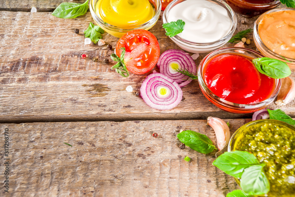 Set of sauces in small bowls - ketchup, mayonnaise, mustard, bbq sauce, pesto, classic burger sauce, with spices and herbs in. Wooden background copy space top view Set of sauces in small bowls - ketchup, mayonnaise, mustard, bbq sauce, pesto, classic burger sauce, with spices and herbs in. Wooden background copy space top view