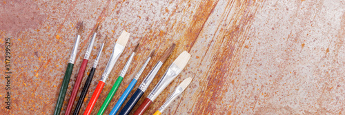 Row of colorful paint brushes are lying on the rusty background. Panoramic image