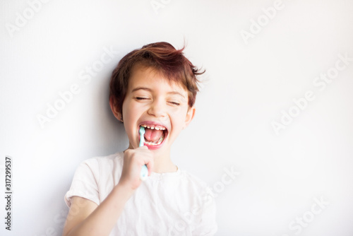 Horizontal portrait of child with closed eyes brushing teeth with blue and white toothbrush. Dental and health care from childhood. Healthy changing teeth on smiling face. Copy space for text