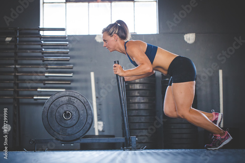 Female fitness model pushing a sled in a cross fit gym.