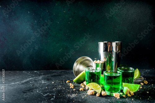 Strong alcohol. Absinthe with sugar, ice cubes and lime slices, Three shot glasses with absinthe. Dark stone background copy space photo