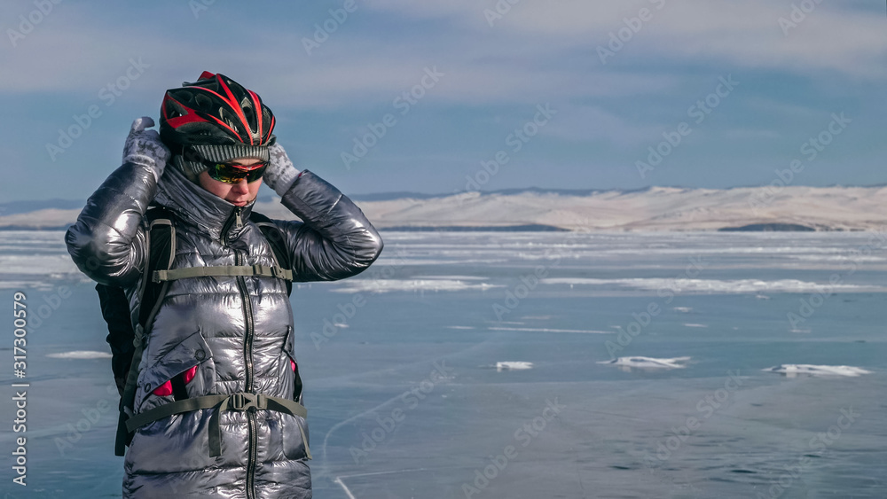 Woman stands near her bike on ice. The girl cyclist stopped to rest. The beautiful view of the sunset. The traveler is ride a cycle. Female is riding bike on the ice. Athlete puts on gear.