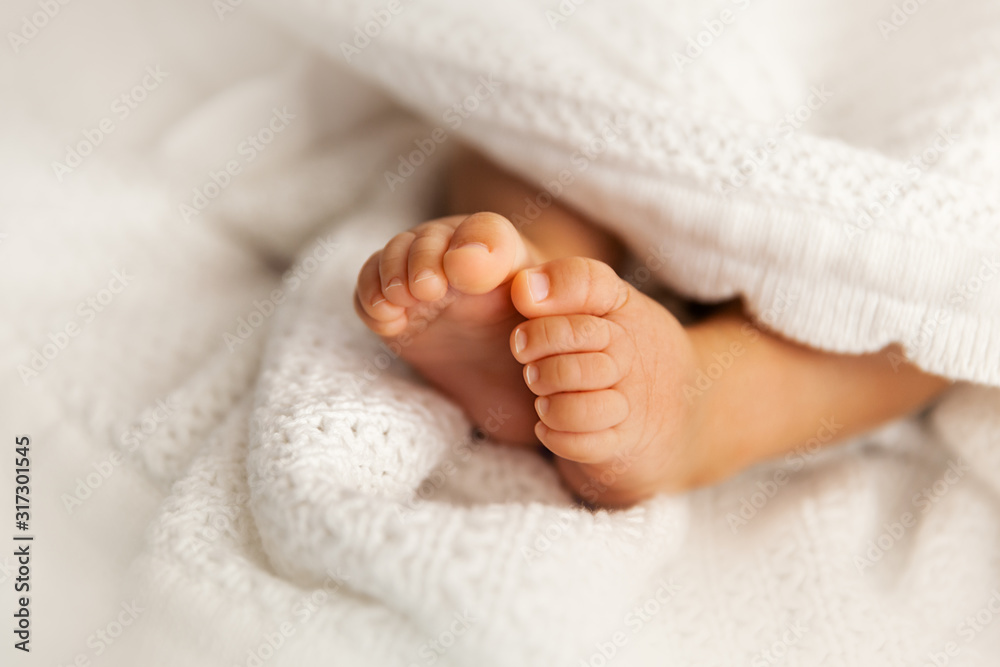 Newborn baby feet under the white blanket, closup of infant barefeet Newborn baby feet under the white blanket, closup of infant barefeet