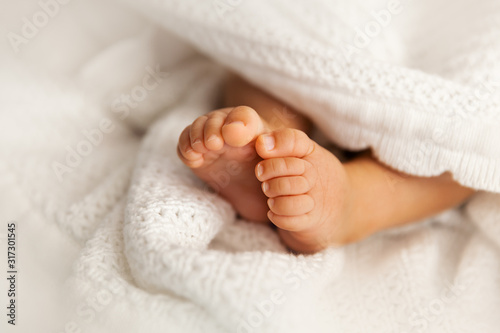 Newborn baby feet under the white blanket, closup of  infant barefeet