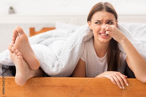 Girlfriend Pinching Nose Lying Near Boyfriend's Smelly Feet In Bed