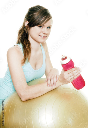young woman holding plastic flask leaning on a fitness ball