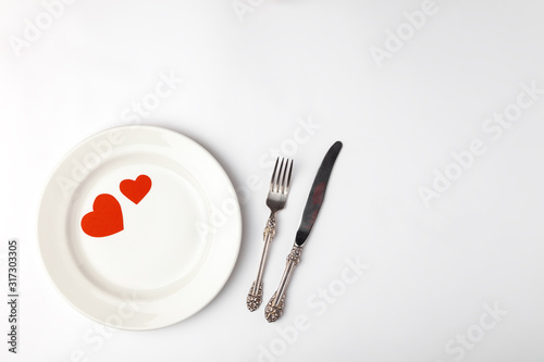 Romantic festive table setting on white background. Valentines day card template. Red paper hearts in ceramic plate  silverware  vintage fork  knife. Place for text  copyspace  top view