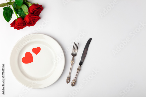 Valentines day dinner with festive table setting, red roses, tape, hearts, ceramic plate, vintage silverware on white background. Top view, space for text, copy space, birthday greeting, anniversary