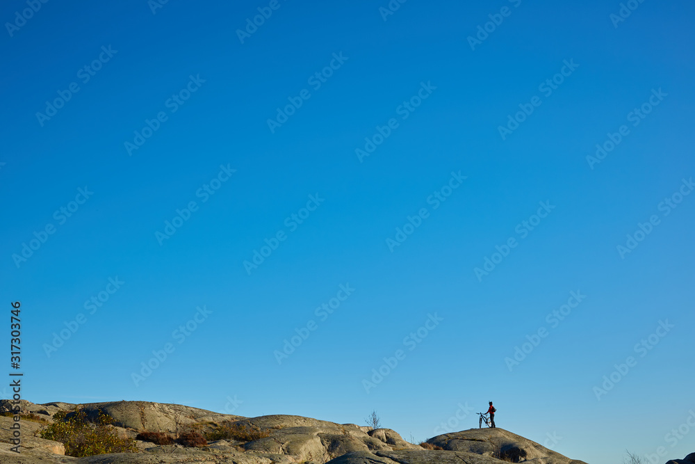 Naklejka premium Silhouette of young active man with bicycle standing and looking forward at mountains panoramic background