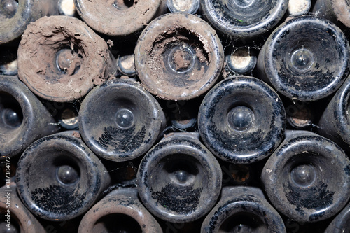 Closeup pattern from bottom of old dark dusty wine bottles in rows in cellar, basement, wine warehouse, winery. Concept vault with old rare wines, exclusive collection rare bottle. Mosaic background