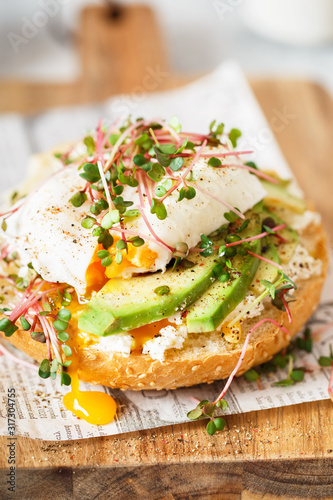Poached egg with avocado, ricotta cheese and radish sprouts on burger bun. Healthy sandwich with bread, fresh avocado, poached egg and cheese garnished with radish microgreens. Healthy eating