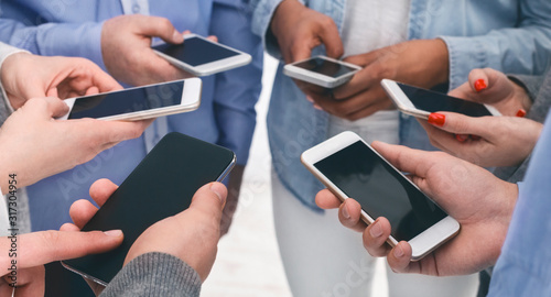 Closeup of diverse people standing in circle holding smartphones photo