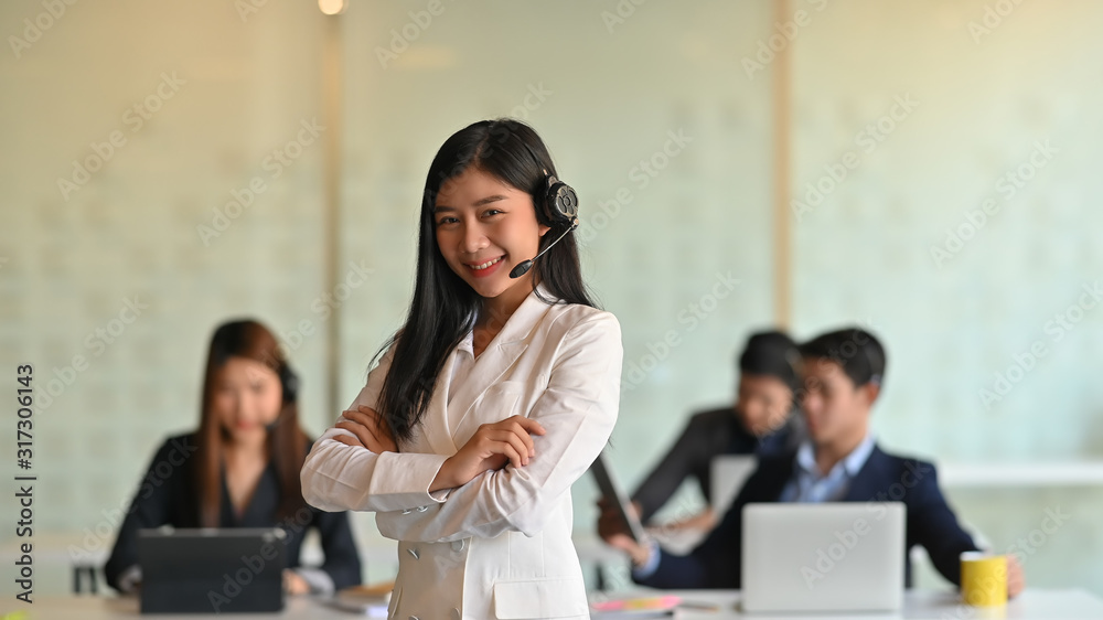Photo of beautiful woman working as leader of call center while she standing and smiling surrounded by her colleague. Photo of beautiful woman working as leader of call center while she standing and smiling surrounded by her colleague.