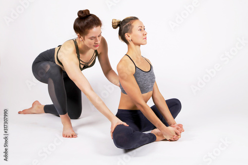 Two young slim european sportswomen attractive girls practicing a yoga lesson with an instructor, standing in an exercise, working out, Studio,Practicing Yoga Class.The concept of rehabilitation