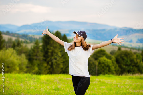 Happy woman in hat stretching to sun after night in tent on top of mountains.
