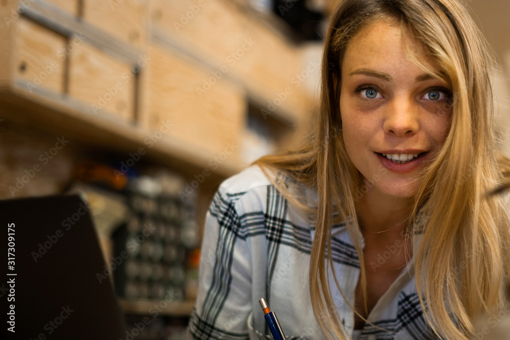 Portrait of smiling young woman writing on notepad while working in workshop Portrait of smiling young woman writing on notepad while working in workshop