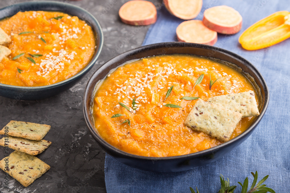 Sweet potato or batata cream soup with sesame seeds and snacks in blue ceramic bowls on a black concrete background. side view, selective focus Sweet potato or batata cream soup with sesame seeds and snacks in blue ceramic bowls on a black concrete background. side view, selective focus