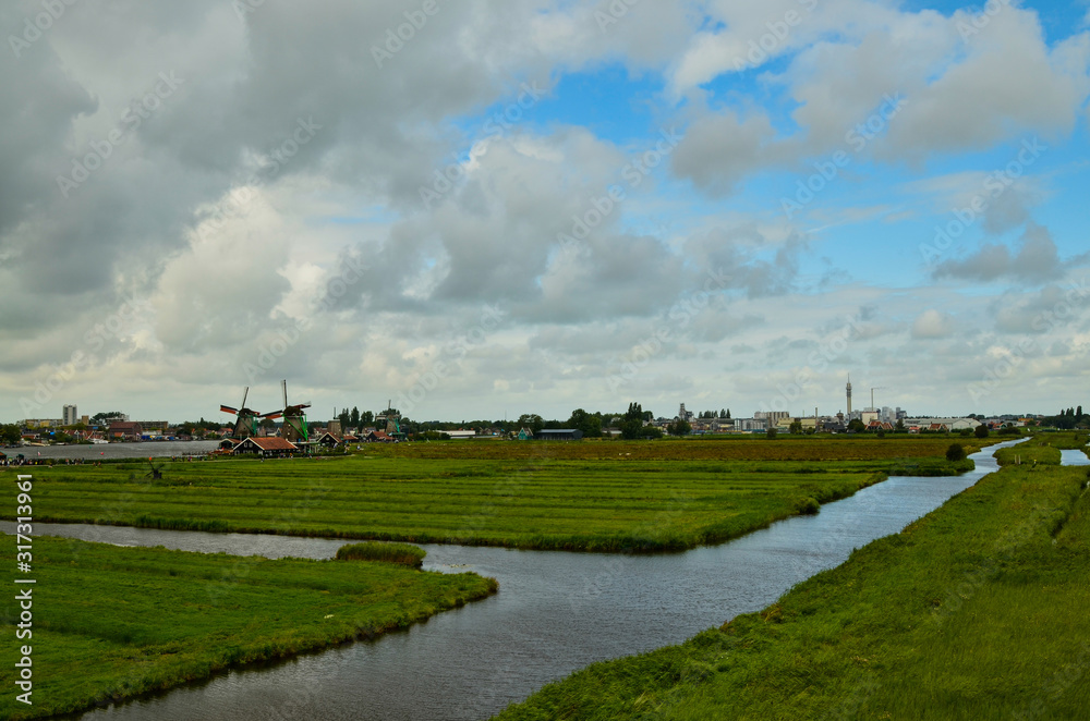 Zaanse Schans, Holland, August 2019. North-east of Amsterdam is a small community located on the quay of the Zaan river. View from above of the fields with mills, tourists are noticed. Cloudy day.