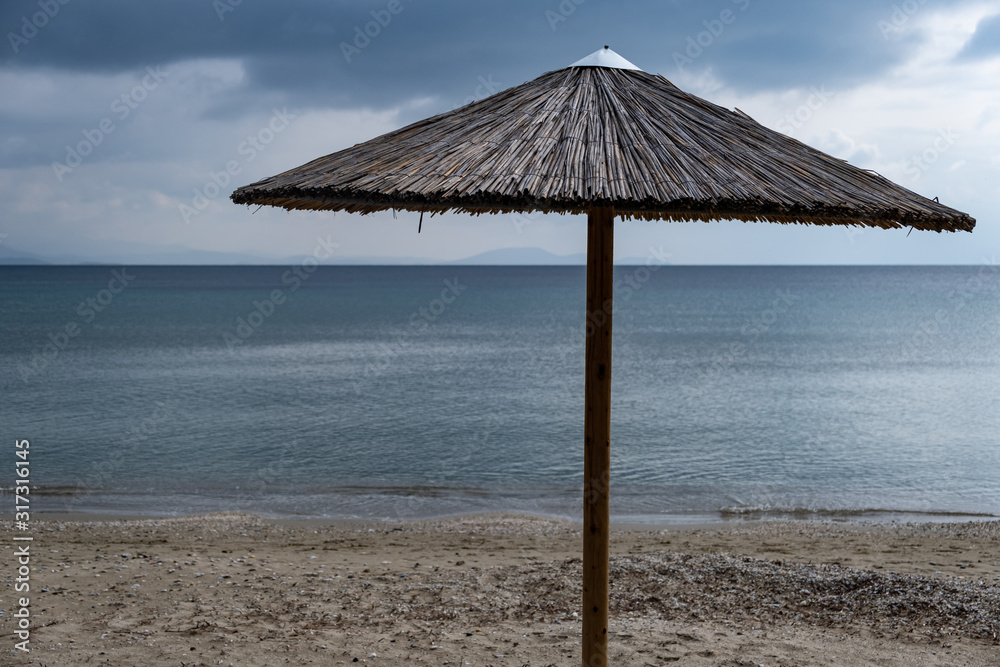Straw umbrella on an empty sandy beach. Dark blue sea and sky background