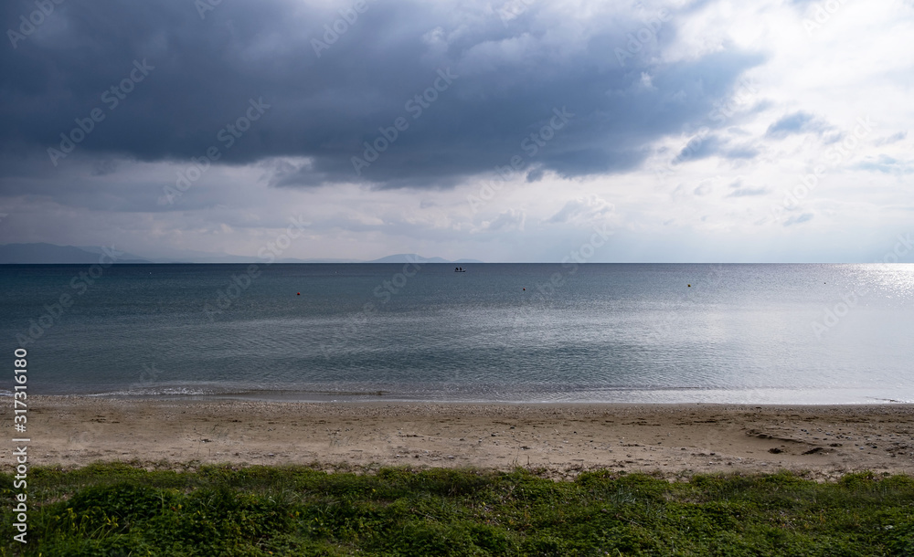 Heavy, fluffy clouds background meet calm dark blue sea far from the sandy coast. Copyspace.