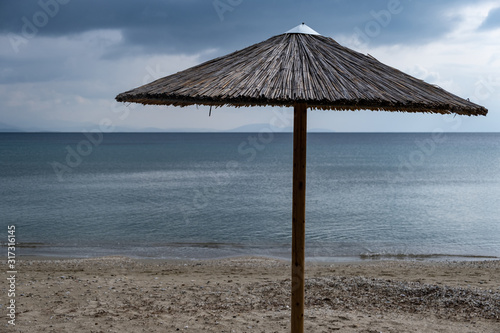 Straw umbrella on an empty sandy beach. Dark blue sea and sky background © Rawf8