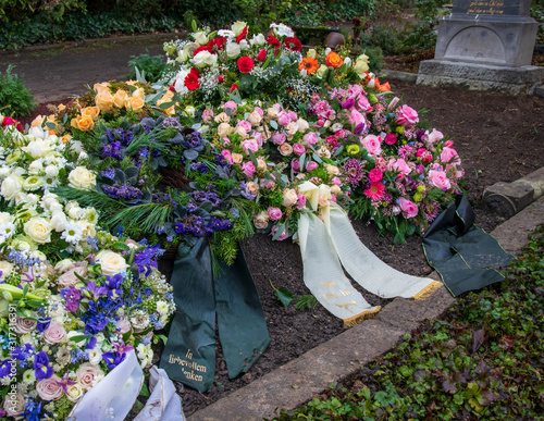 Viele bunte Kränze mit Schleifen auf einem Grab