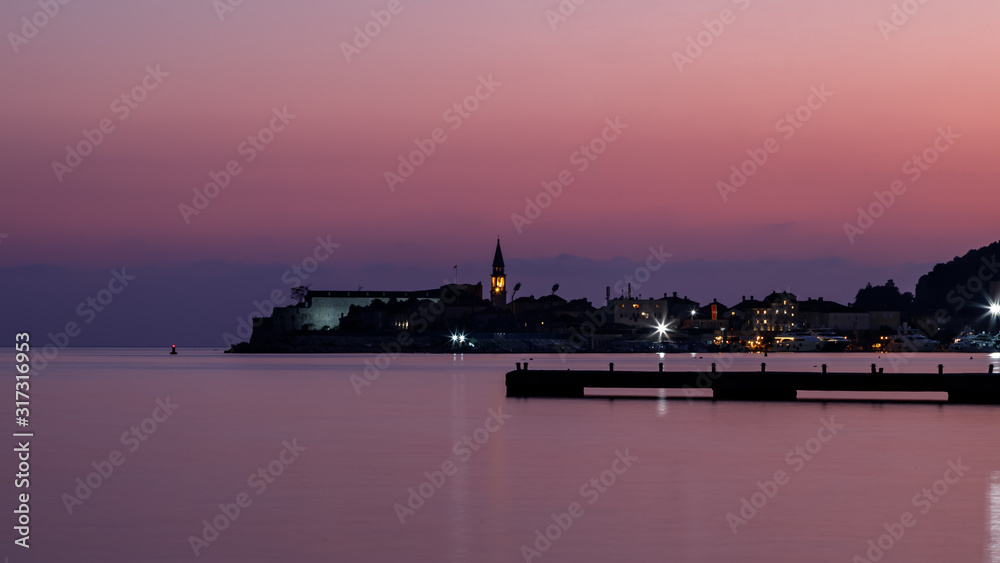 Night silhouette view of Budva old town, pier and harbour, Montenegro. City skyline, pink sky and water.