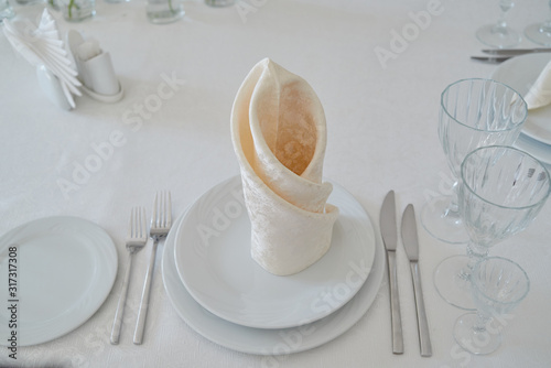 Table setting with white plates, napkins, wineglasses, cutlery and flowers on table, copy space. Place setting at wedding reception. Table served for wedding banquet in restaurant