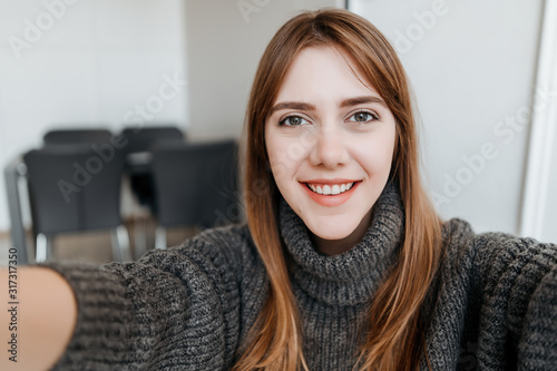 young millennial beautiful woman making selfie at home in apartment