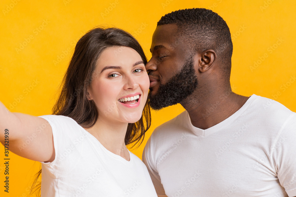 Fototapeta premium Romantic multiracial couple taking selfie, loving black guy kissing his girlfriend