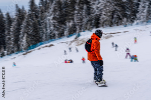 Back view of unrecognizable male in bright ski suit moving down on snowboard in motion blurred