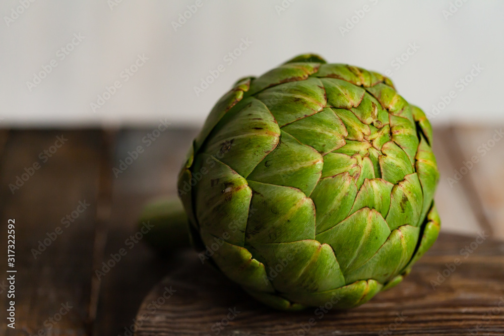 Fototapeta premium Fresh green artichoke on rustic wooden background. Minimalism. Concept of healthy and not boring vegetarian food. Close up, macro