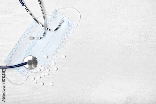 Creative flat lay overhead composition with stethoscope, disposable face masks and scattered pills on a light wooden background. Top view. Free copy space for text