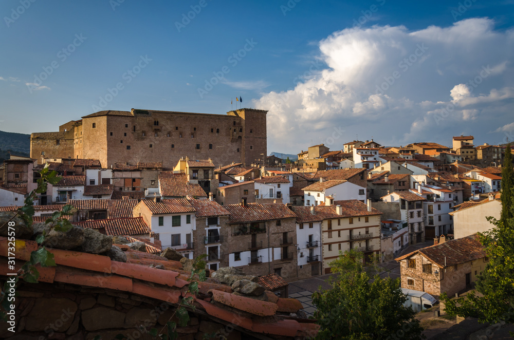 A panoramic view at sunset of the medieval village of Mora de Rubielos with a tile roof in the foreground and the great castle on the left in the background, Teruel, Spain