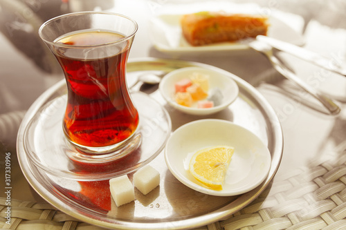 Turkish tea in traditional glass on metal tray with baklava, sugar, lemon and succades. Close up. Outdoor shot
