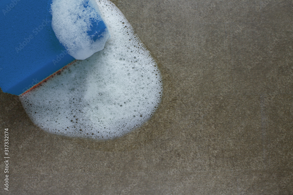 Obraz premium Cleaning green sponge with white foam on a gray-brown surface close-up with copy space. Concept-clean