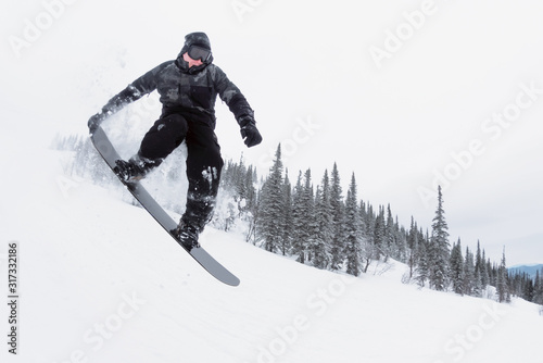 Amateur snowboarder is jumping from small kicker in the winter forest.