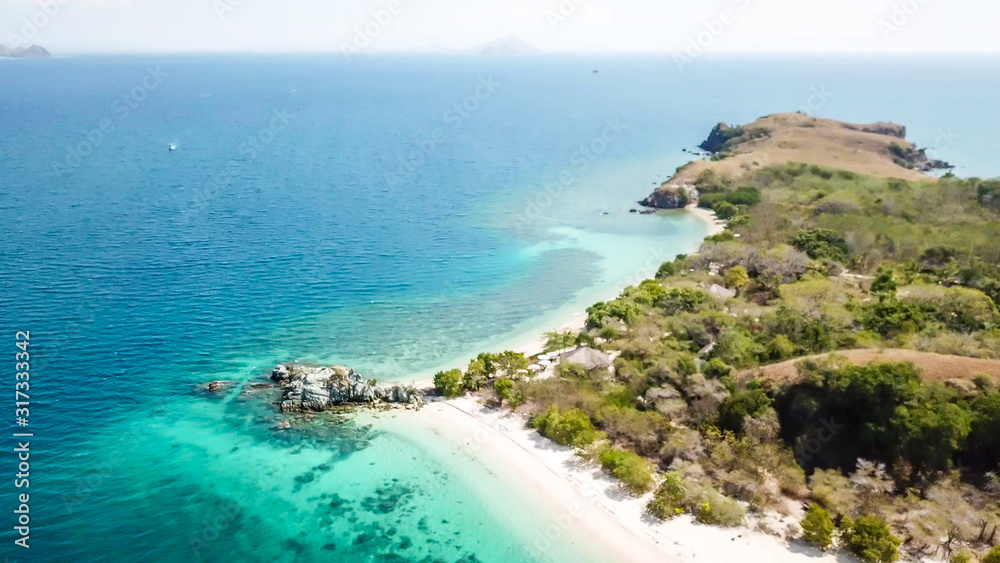 A drone shot of a paradise island with some boats anchored around in Komodo National Park, Flores, Indonesia. Green middle part of the island turns into white sand beach and further into turquoise sea