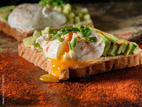 Toasts with avocado and poached egg on a dark background, sprinkled with ground pepper, closeup