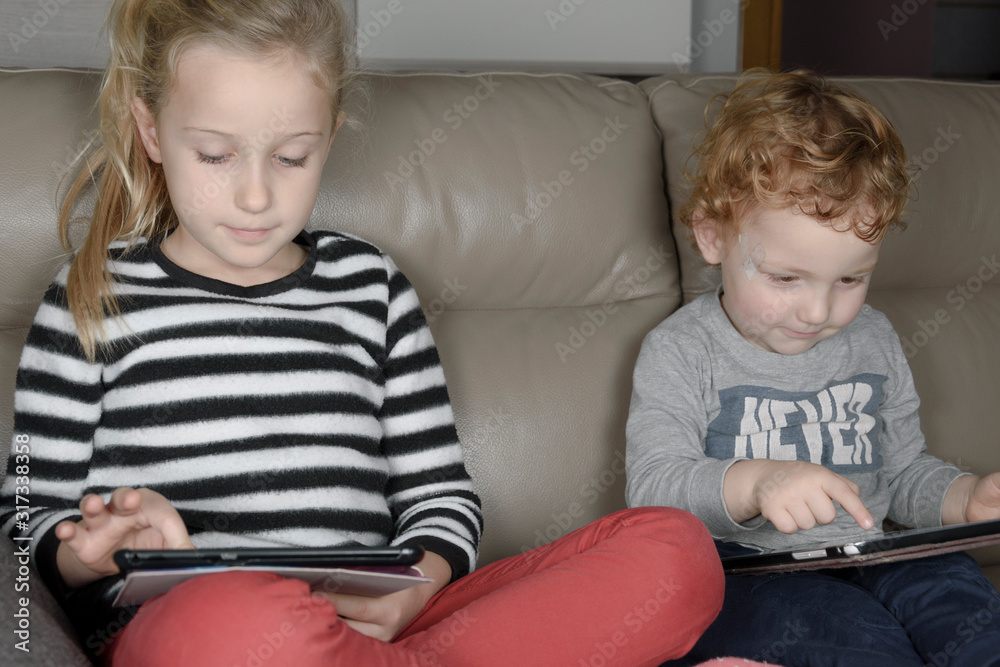Kids sitting in sofa and playing with tablet. Sister and brother have fun with digital tablets on sofa at home. Communication and family friendship concept. Kids sitting in sofa and playing with tablet. Sister and brother have fun with digital tablets on sofa at home. Communication and family friendship concept.