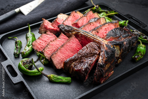 Barbecue dry aged wagyu porterhouse beef steak with large fillet piece sliced as closeup on a black modern design tray with green chili photo