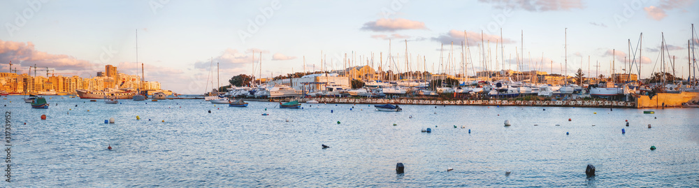 Sunset panorama view of Marsamxett harbour. Many sailing yachts moored on pier. Seashores of Sliema and Valletta, Malta.