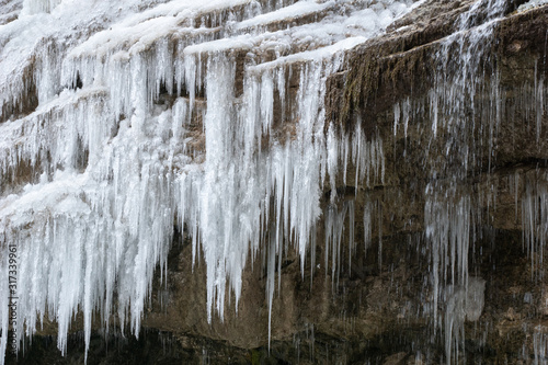 icicles from the jets of a frozen waterfall on a brown rock. winter in caucasian mountains