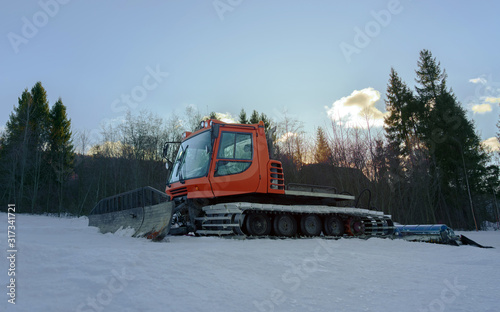 Snow groomer machine on ski track ready to work at sunrise