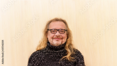 A stylish, happy, elderly man with glasses who looks like an old woman, an old man with long gray hair and a black sweater. Close-up portrait of a white-bearded smiling man. Billet for advertising.