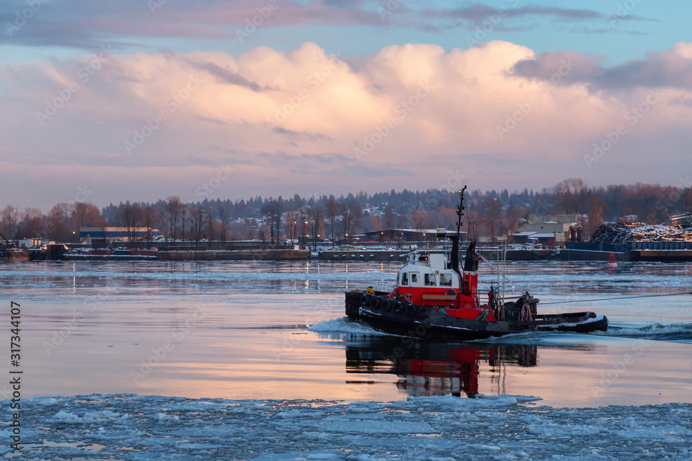 Industrial Tugboat pulling a load in Fraser River during a colorful winter sunset with ice in the water. Taken in New Westminster, Vancouver, BC, Canada. Industrial Tugboat pulling a load in Fraser River during a colorful winter sunset with ice in the water. Taken in New Westminster, Vancouver, BC, Canada.