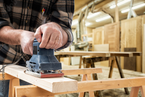 Close-up. Carpenter with the electric sander smoothes a wooden board. Construction industry, carpentry workshop.