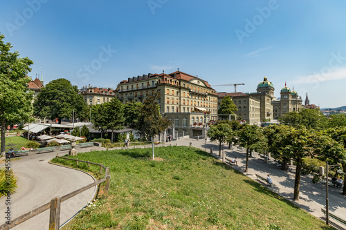Bern, Switzerland - July 26, 2019: Federal government office and west wing of the Federal Palace of Switzerland. Swiss capital parliament building with green dome roof and Swiss flag in old town Bern