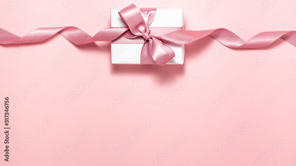 White gift box with a purple satin ribbon bow on pink flat lay White gift box with a purple satin ribbon bow on pink flat lay