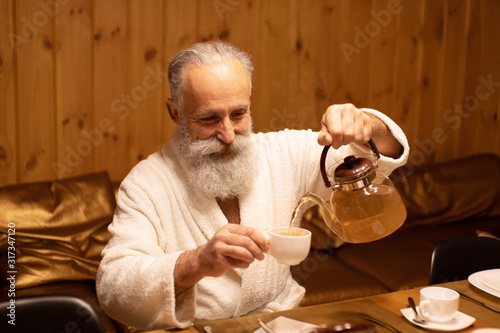 Bearded senior man drink tea after the procedure in the sauna. Concept - healthy lifestyle.